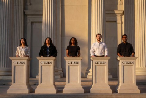 Five different citizens stand behind identical podiums labelled “Citizen” in front of classical columns.